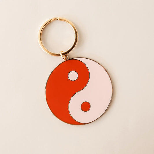 Vibrant 'Yin-Yang' keychain with contrasting deep red and pale pink halves. The design has a golden border and metallic gold key ring.