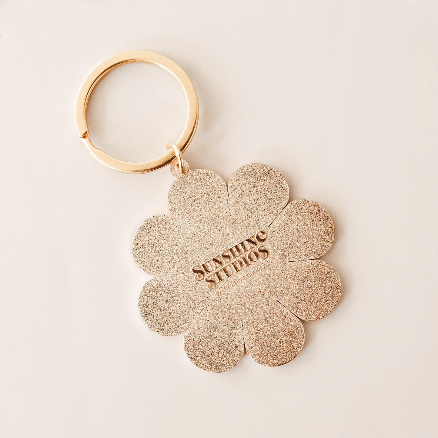Back of the retro flower keychain. The back is textured and reads 'sunshine studios' in raised lettering.