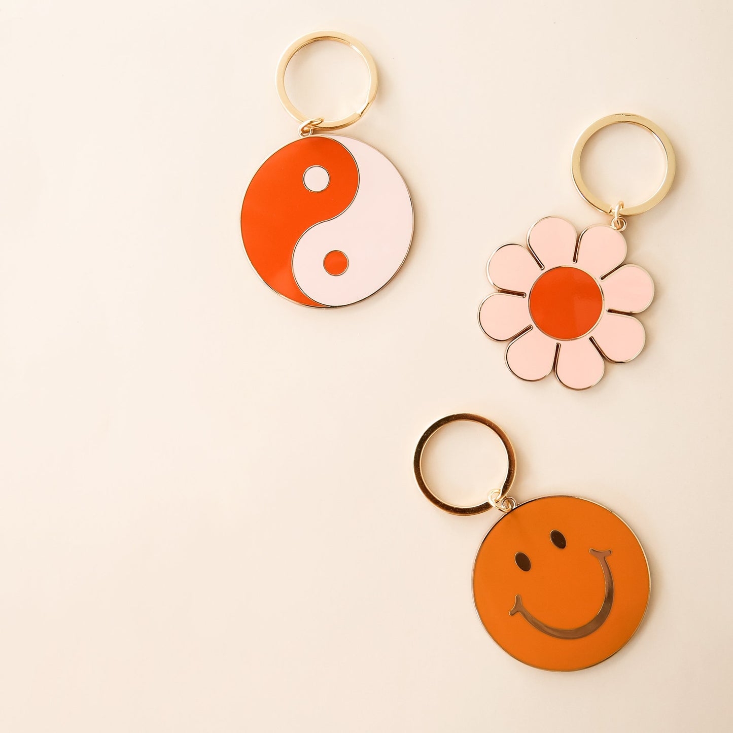 Three keychains including a yin-yang symbol, flower and smiley face. Each keychain has gold detailing and a golden key ring.
