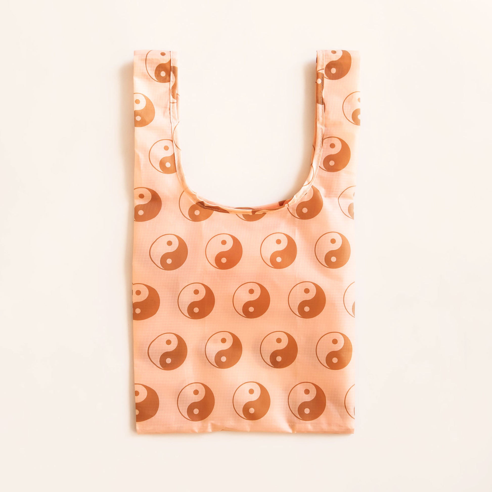 Peach reusable bag filled with a pattern of brown and peach yin-yang symbols. The bag is positioned flat on a table and has a 'U' shape between two handles.