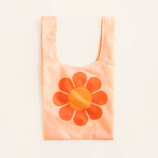 Peach reusable bag featuring a large bus flower with red-orange petals and tangerine center. The flower is positioned in the center of the bag. The bag is positioned flat on a table and has a 'U' shape between two handles.