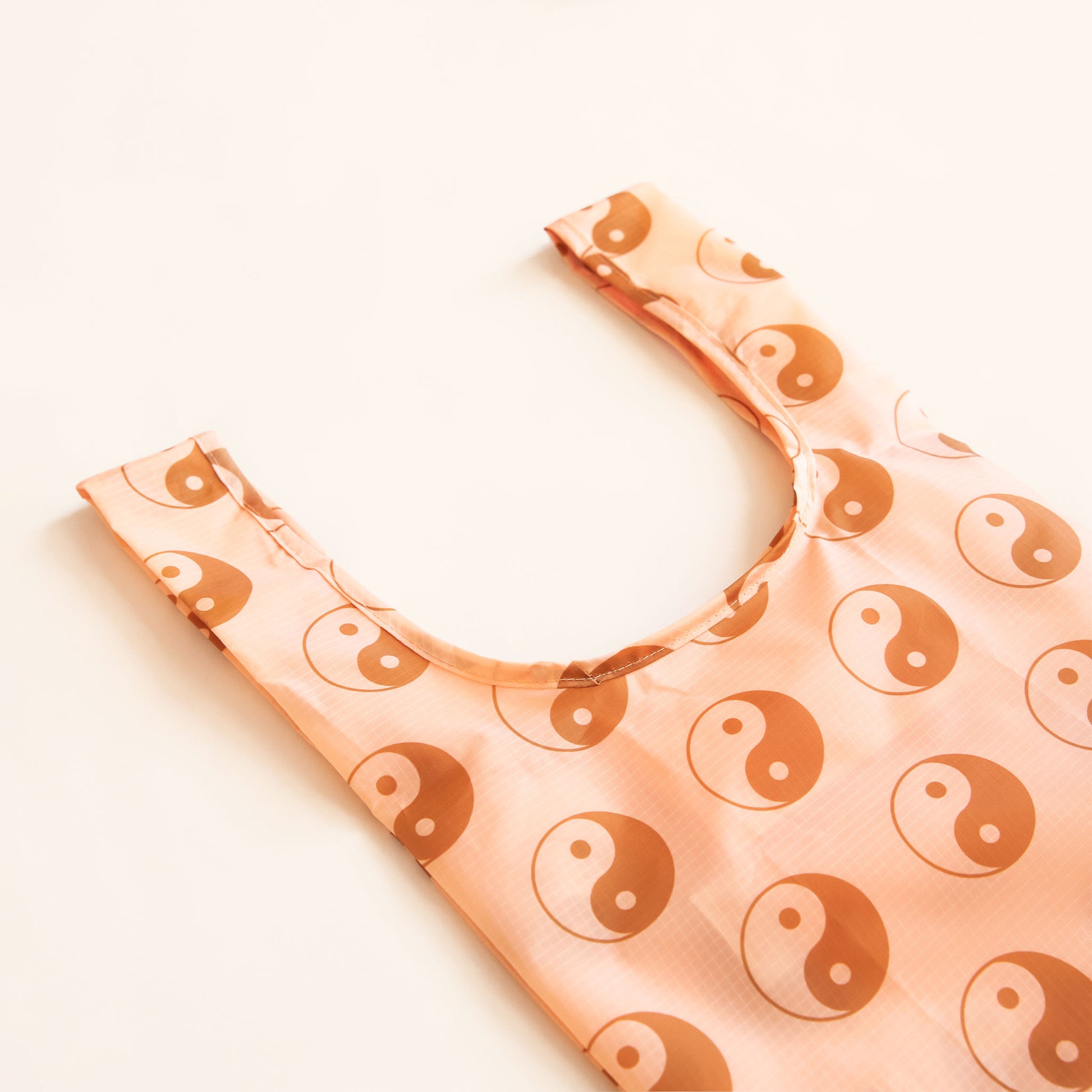 Peach reusable bag filled with a pattern of brown and peach yin-yang symbols. The bag is positioned flat on a table and has a 'U' shape between two handles. 