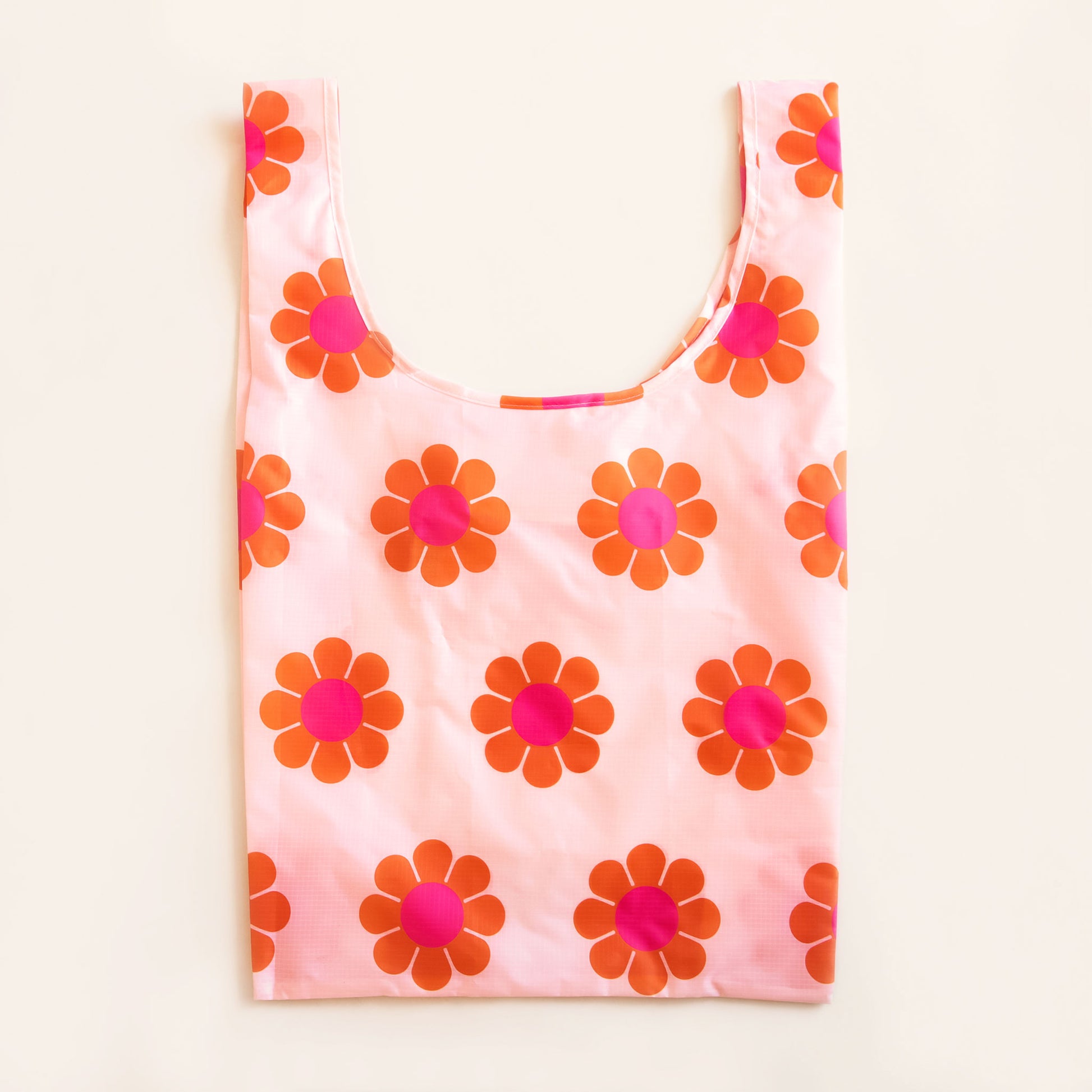 Peach reusable bag covered in a print of simple flowers with red-orange petals and magenta centers. The bag is positioned flat on a table and has a 'U' shape between two handles.