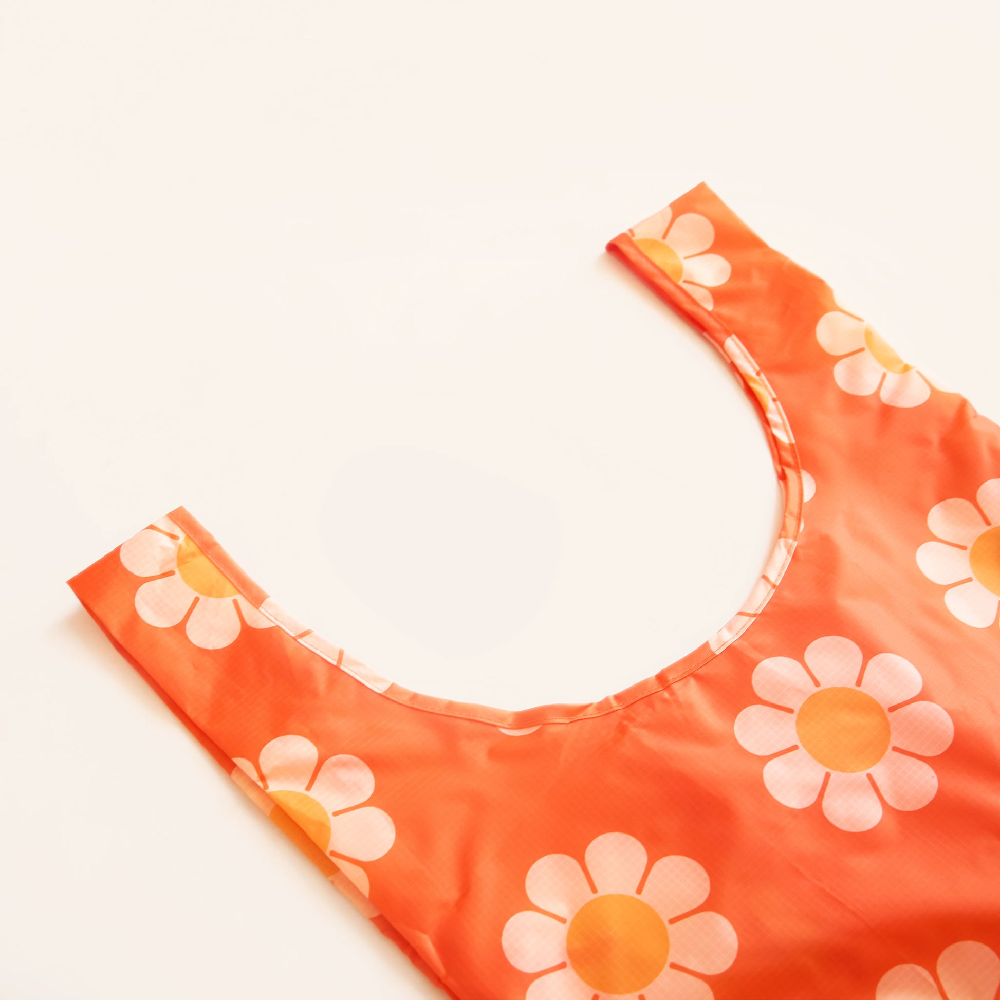 Zoomed view of red-orange nylon reusable bag. The bag is covered in a print of large simple flower with white petals and orange centers. 
