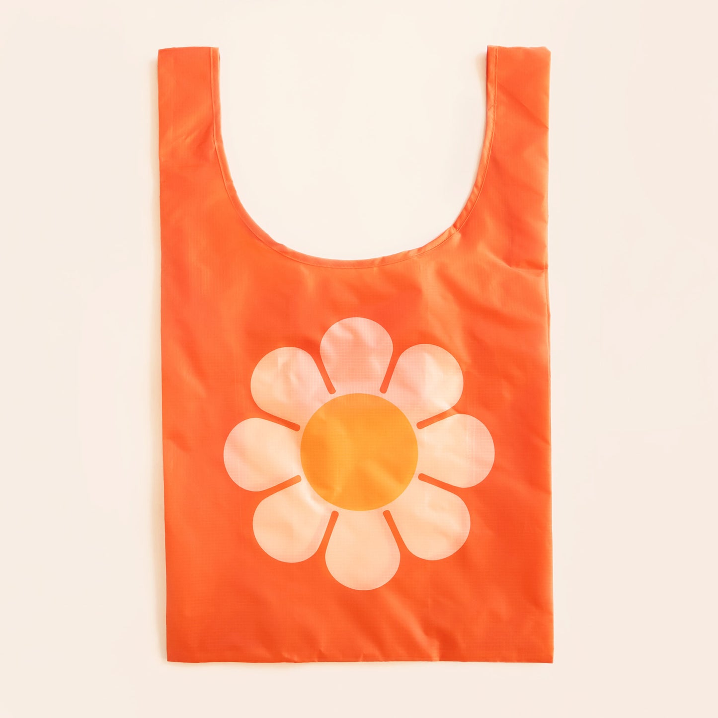 Orange reusable bag featuring a large bus flower with peach petals and tangerine center. The flower is positioned in the center of the bag. The bag is positioned flat on a table and has a 'U' shape between two handles.