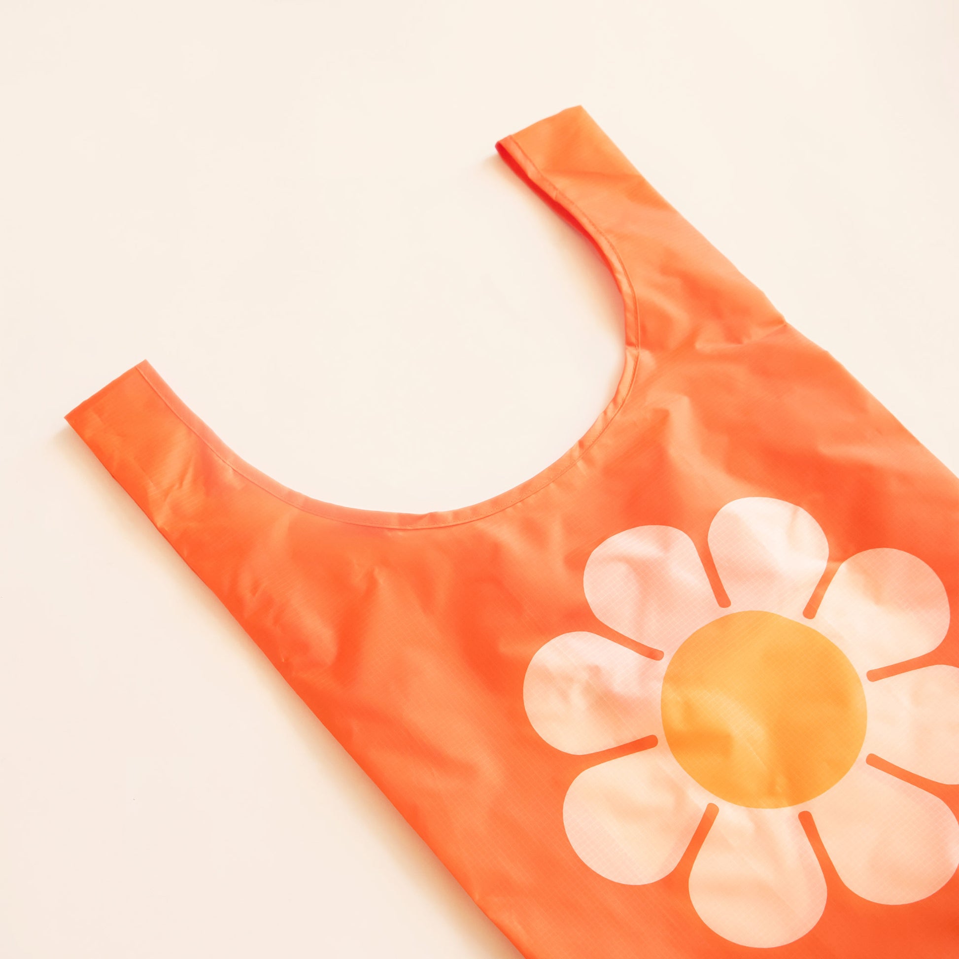 Orange reusable bag featuring a large bus flower with peach petals and tangerine center. The flower is positioned in the center of the bag. The bag is positioned flat on a table and has a 'U' shape between two handles.