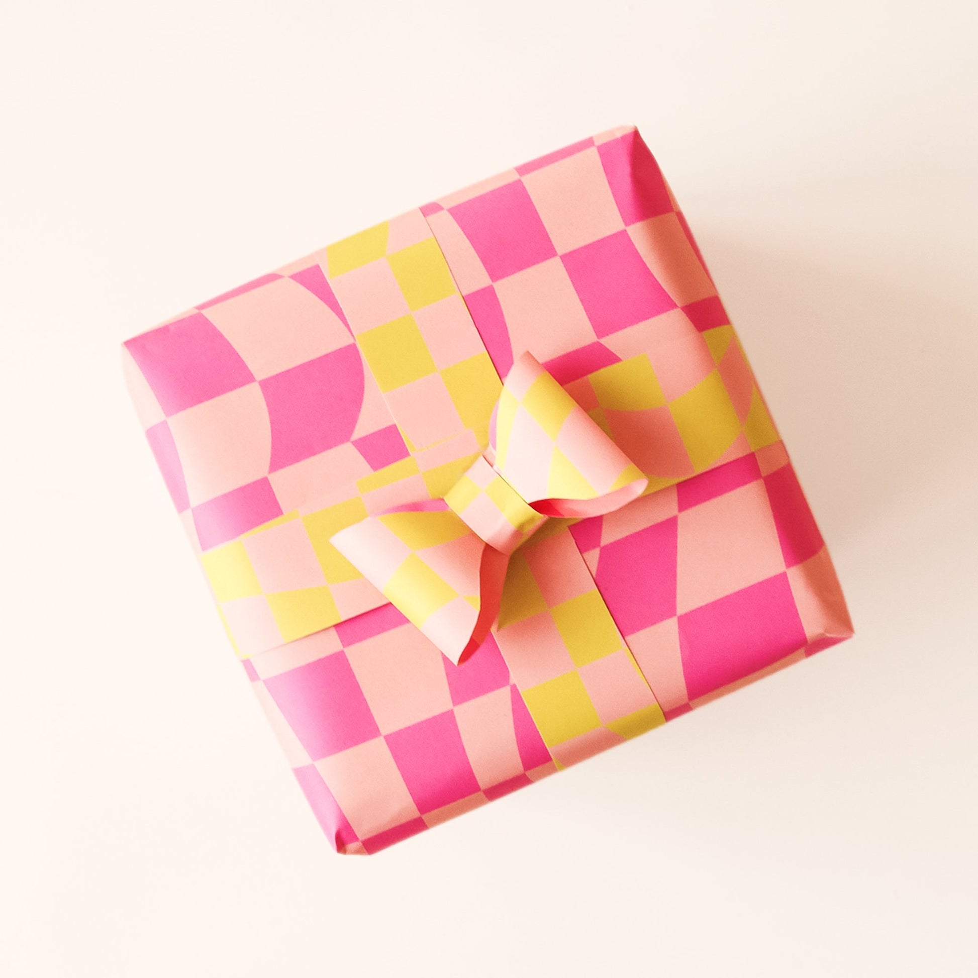 Wrapped present covered in distorted pink checkered wrapping paper. Thin strips of yellow and pink checkered wrapping paper stretch around the present and fasten into a bow.