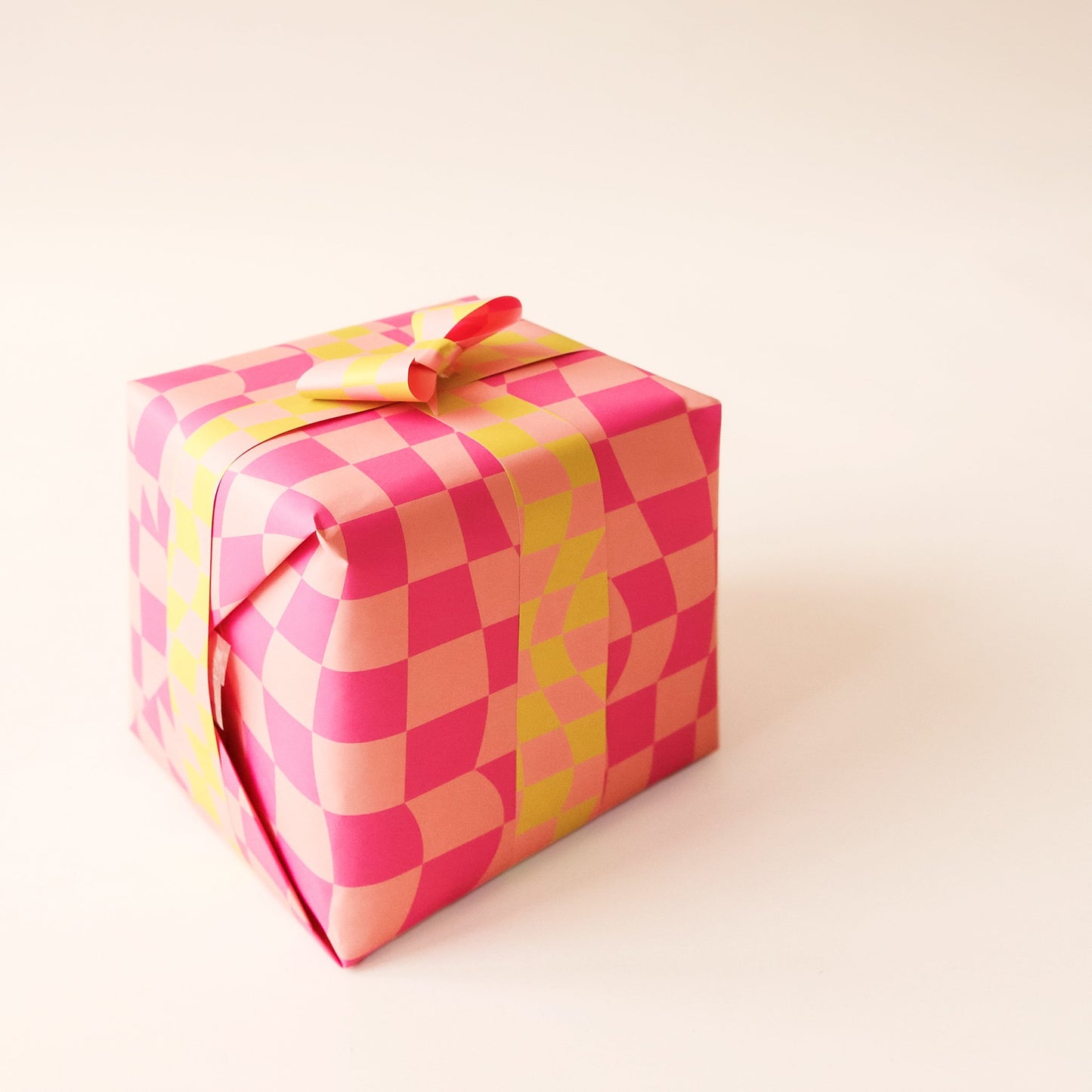 Wrapped present covered in distorted pink checkered wrapping paper. Thin strips of yellow and pink checkered wrapping paper stretch around the present and fasten into a bow.