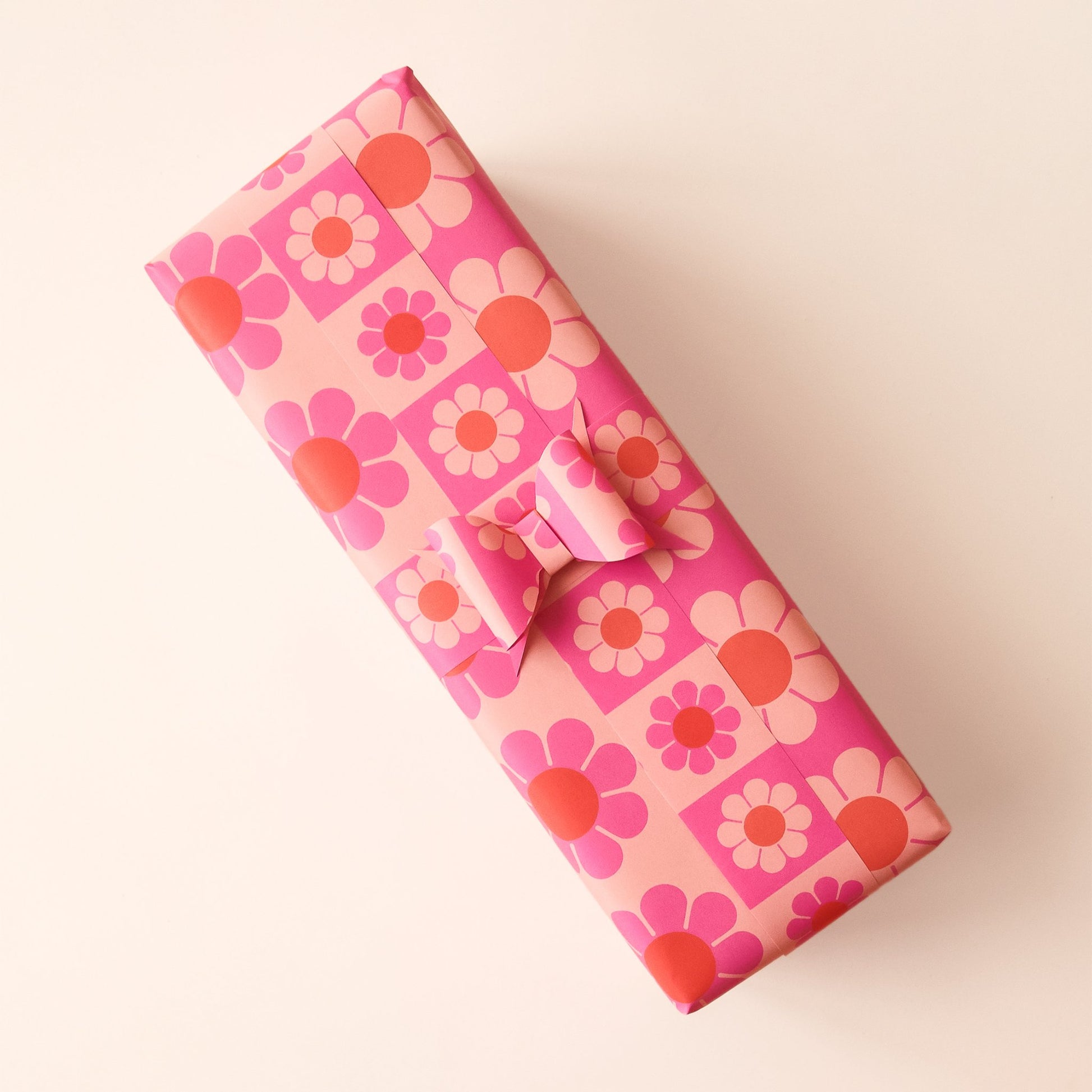 Wrapped present covered in pink and orange flower wrapping paper. Thin strips of wrapping paper with smaller flower print stretch around the present and fasten into a bow.