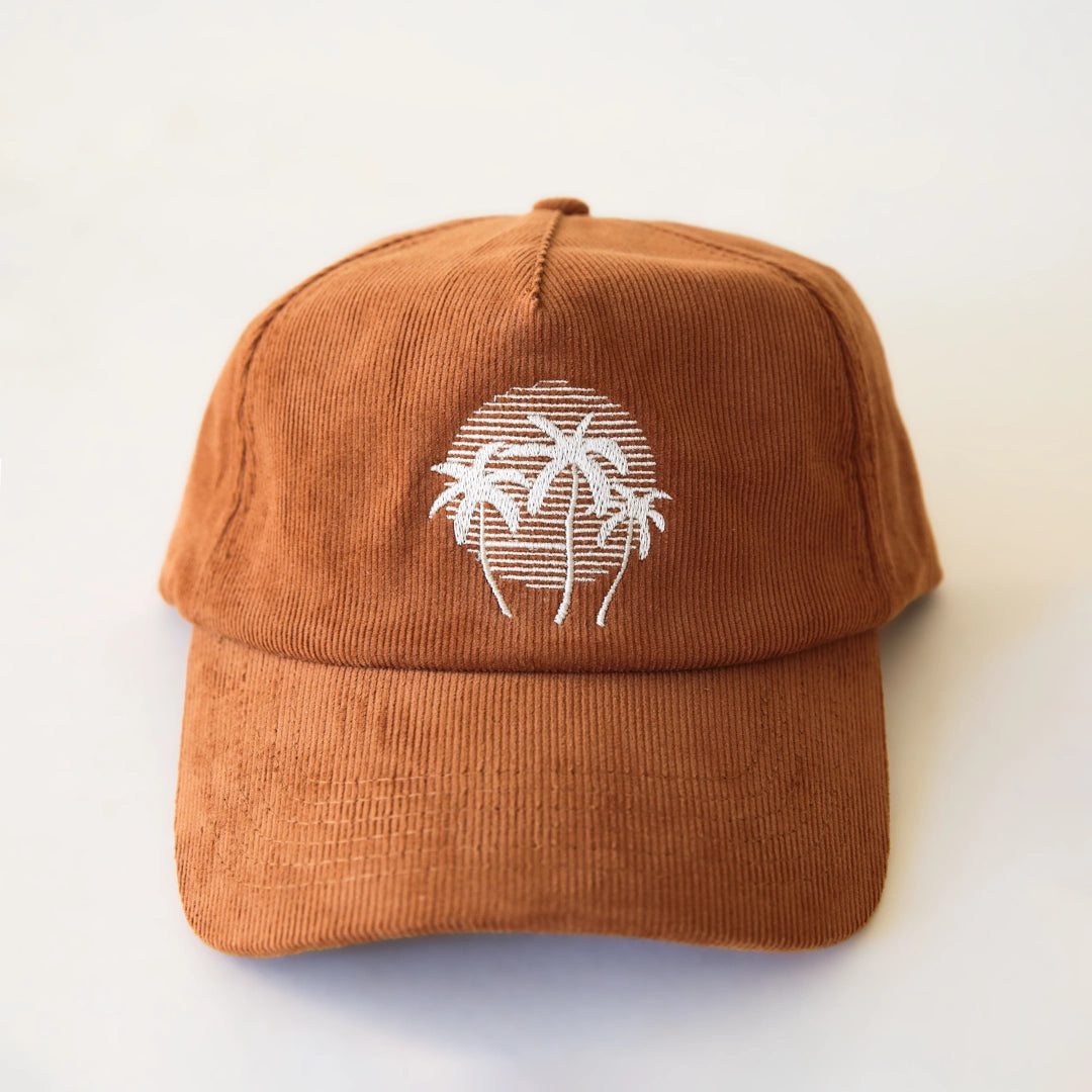 A terracotta colored corduroy baseball hat with a palm tree graphic in the center.