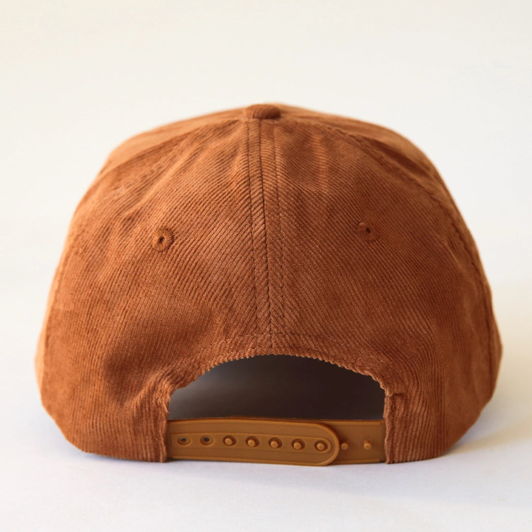 A terracotta colored corduroy baseball hat with a palm tree graphic in the center.