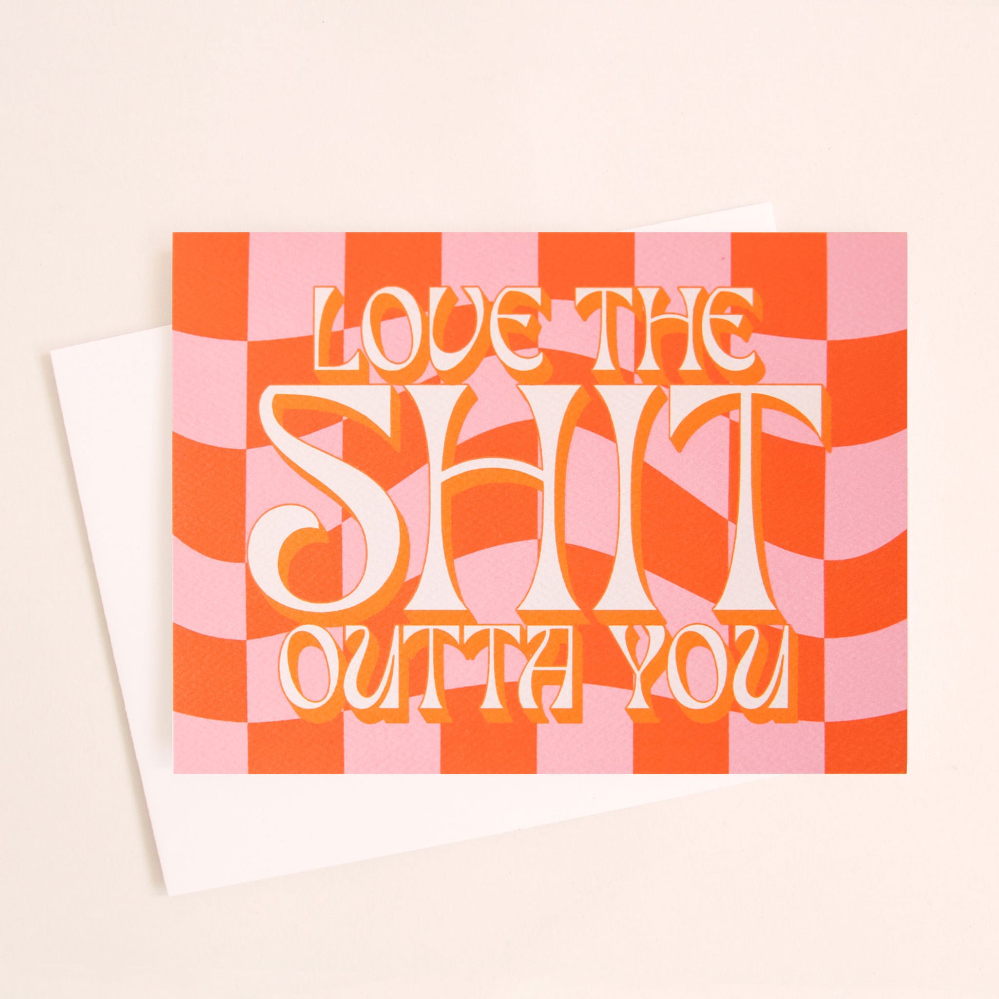 Pink and orange checkered card that reads 'Love the shit our you' in white retro lettering with a tangerine orange shadow. The card is accompanied by a solid white envelope.