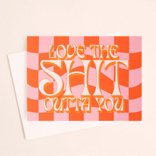 Pink and orange checkered card that reads 'Love the shit our you' in white retro lettering with a tangerine orange shadow. The card is accompanied by a solid white envelope.