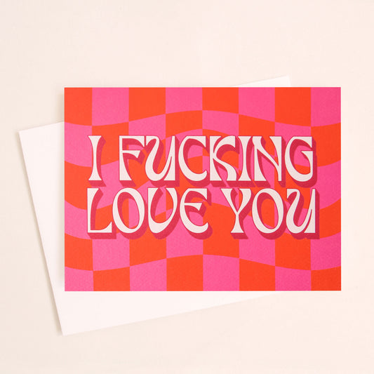 Magenta and red checkered print card that reads 'I fucking love you' in retro white lettering with a thin magenta shadow. The card is accompanied with a white envelope.  