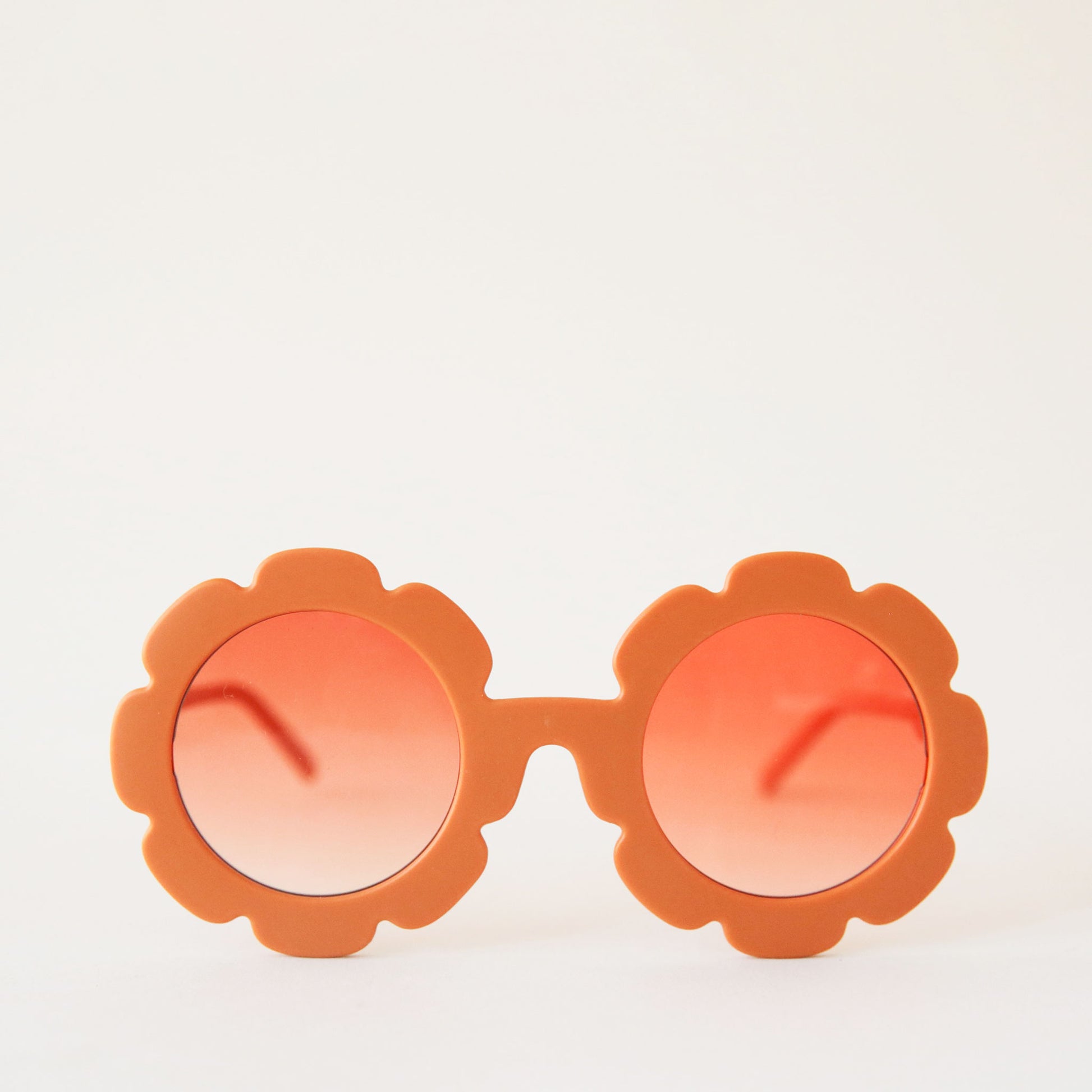 On a white background is a pair of orange, flower shaped sunglasses with a light orange lens. 