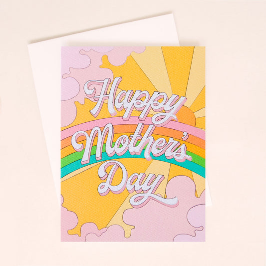 Card with a vibrant scene of a rainbow and beaming yellow sun. Soft lavender clouds take up the edges. The center of the card reads 'Love You Mom' in white cursive lettering with a pink shadow.