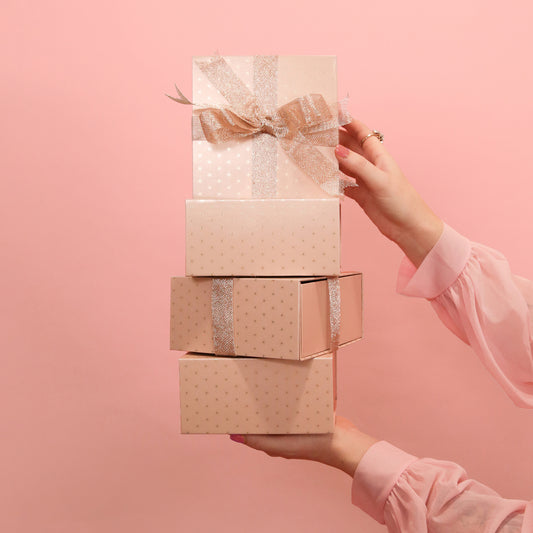 In front of a pink background is four light pink gift boxes with a gold foiled star design on four of the sides, the other sides are solid pink. The gift boxes are accented with a sparkle ribbon tied in a bow, not included with purchase. 