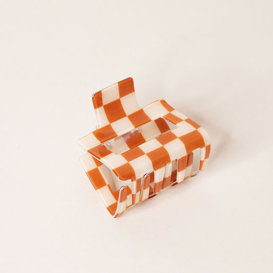 Small orange and white checkered claw hair clip with a square shape and two simple geometric cutouts.