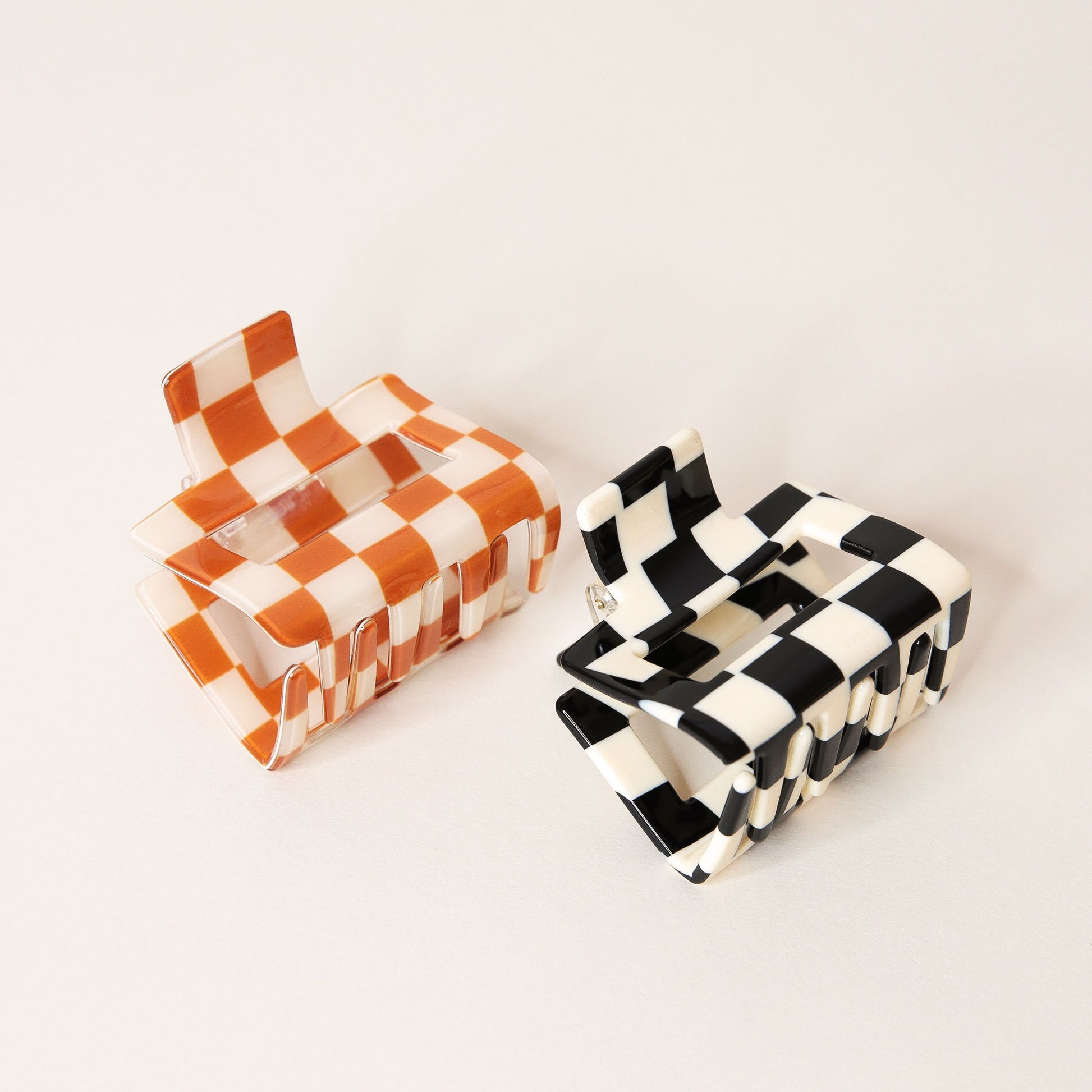 Two checkered claw hair clips in shades of orange and black. Each is a square shape and has two simple geometric cutouts.
