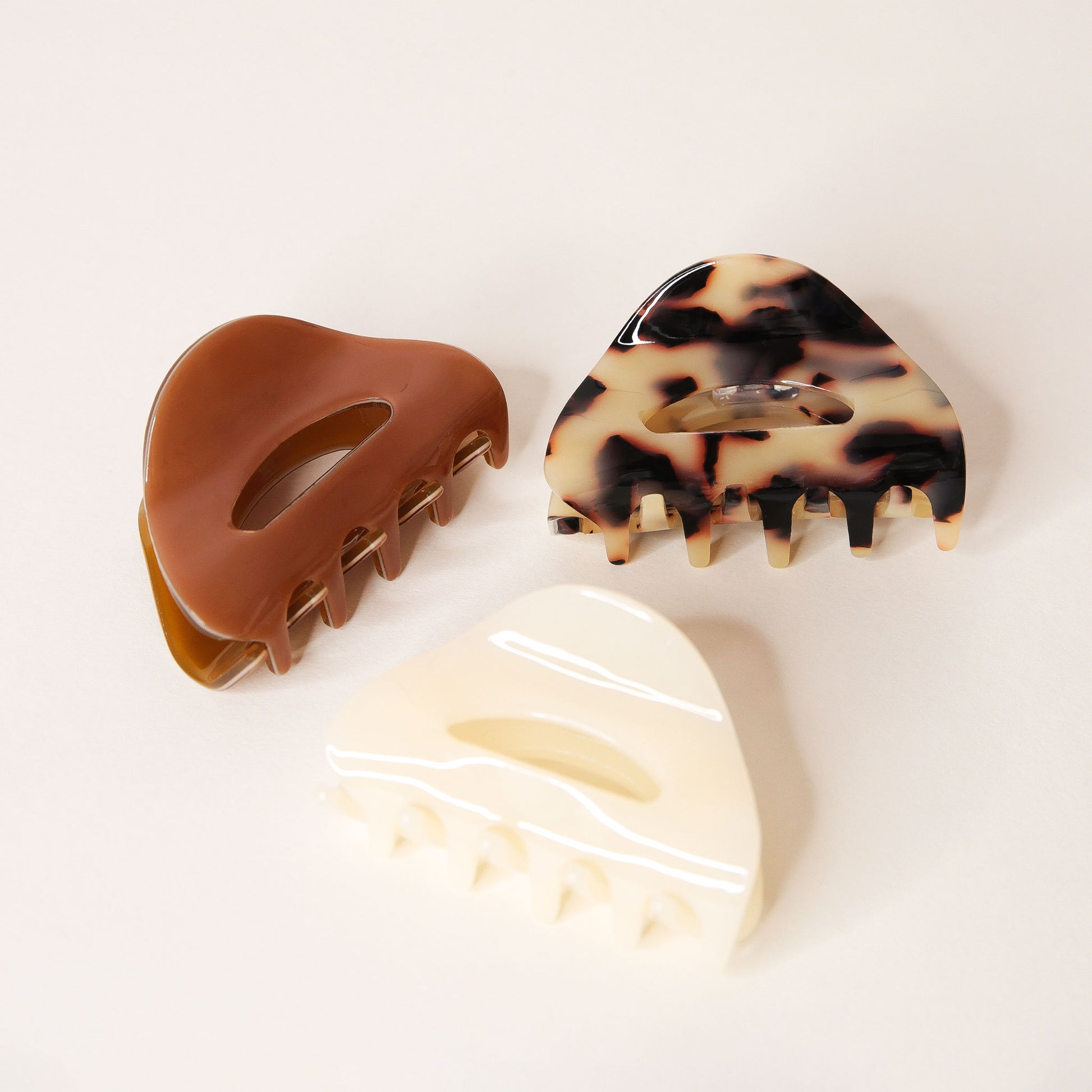 Three round claw hair clips and two simple oval cutouts. The clips are chocolate brown, cream and tortoise. 