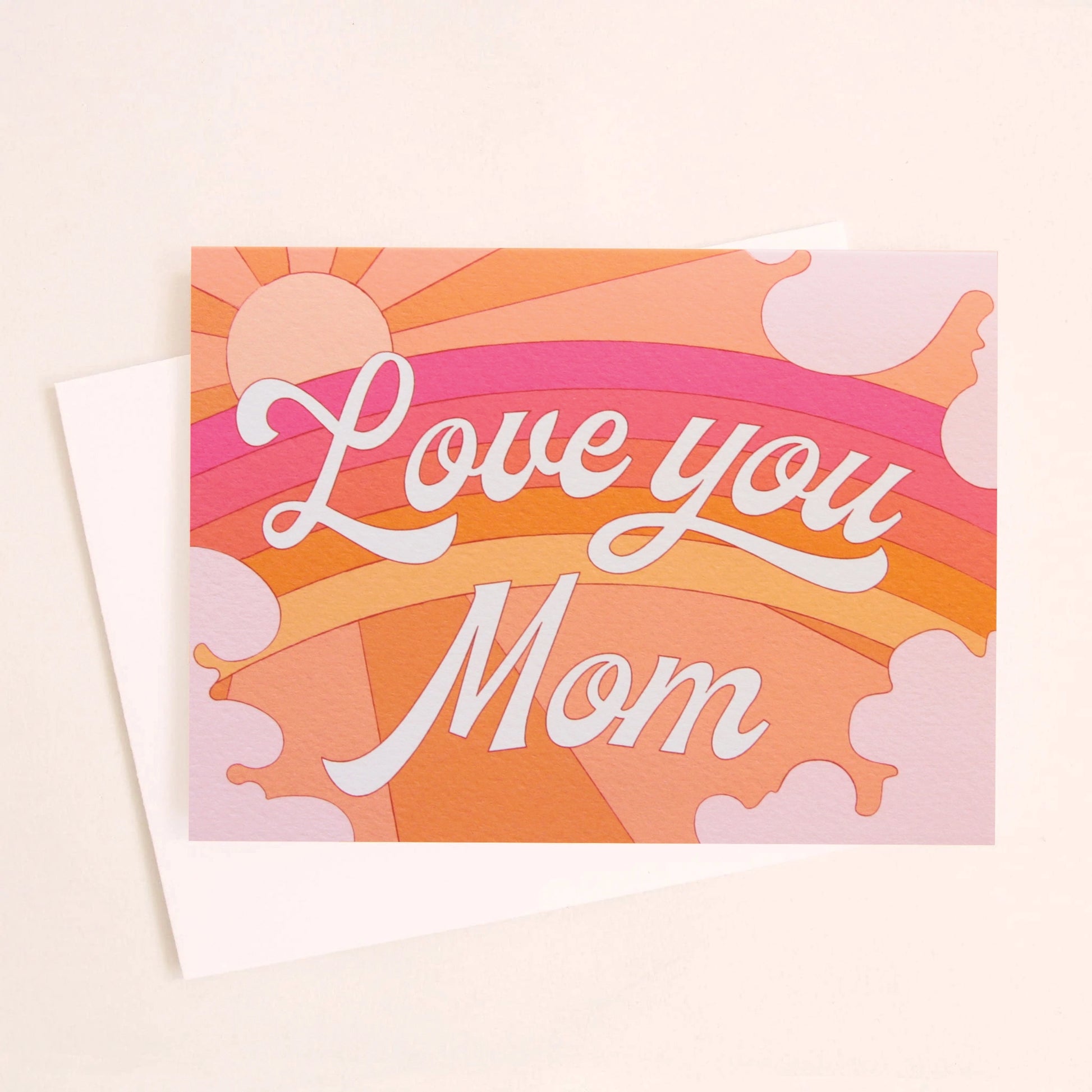 A card with a rainbow graphic made with shades or orange, pink and red along with a shining sun, subtle clouds around the edge and white cursive text that reads, "Love you Mom" in the center as well as a white envelope.