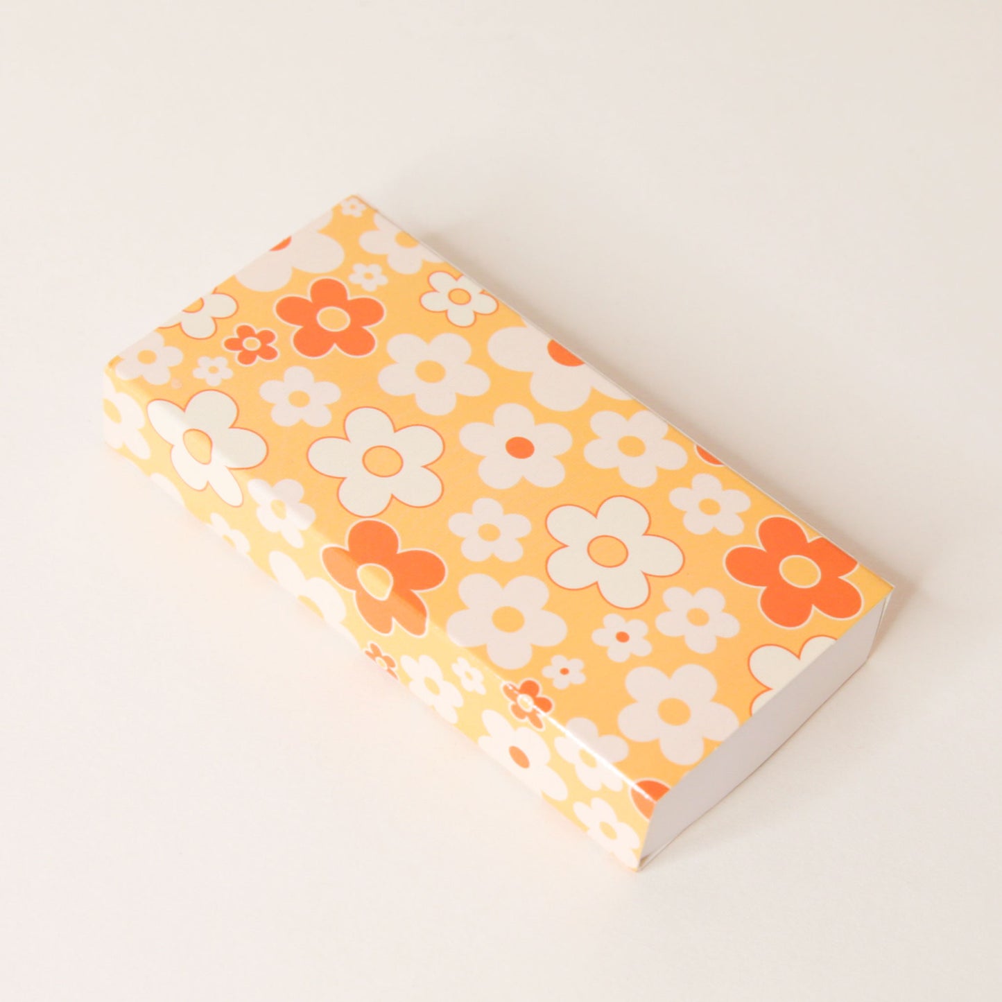 Rectangular match box covered in a flower pattern filled with yellow oranges and whites.