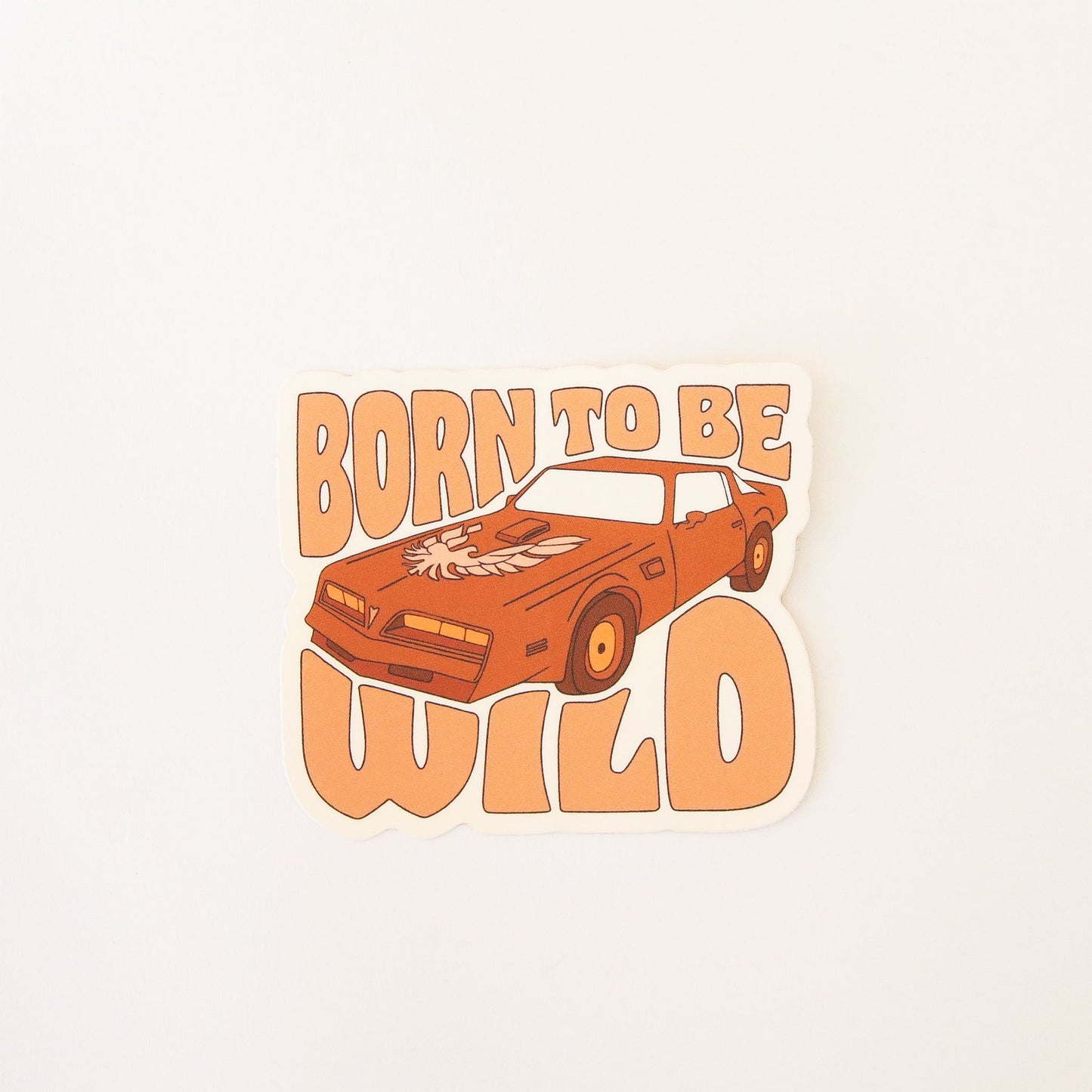 70s inspired sticker featuring an old school Ford Thunderbird car. Wrapped around the car reads 'Born to be wild' in soft orange bubble lettering.