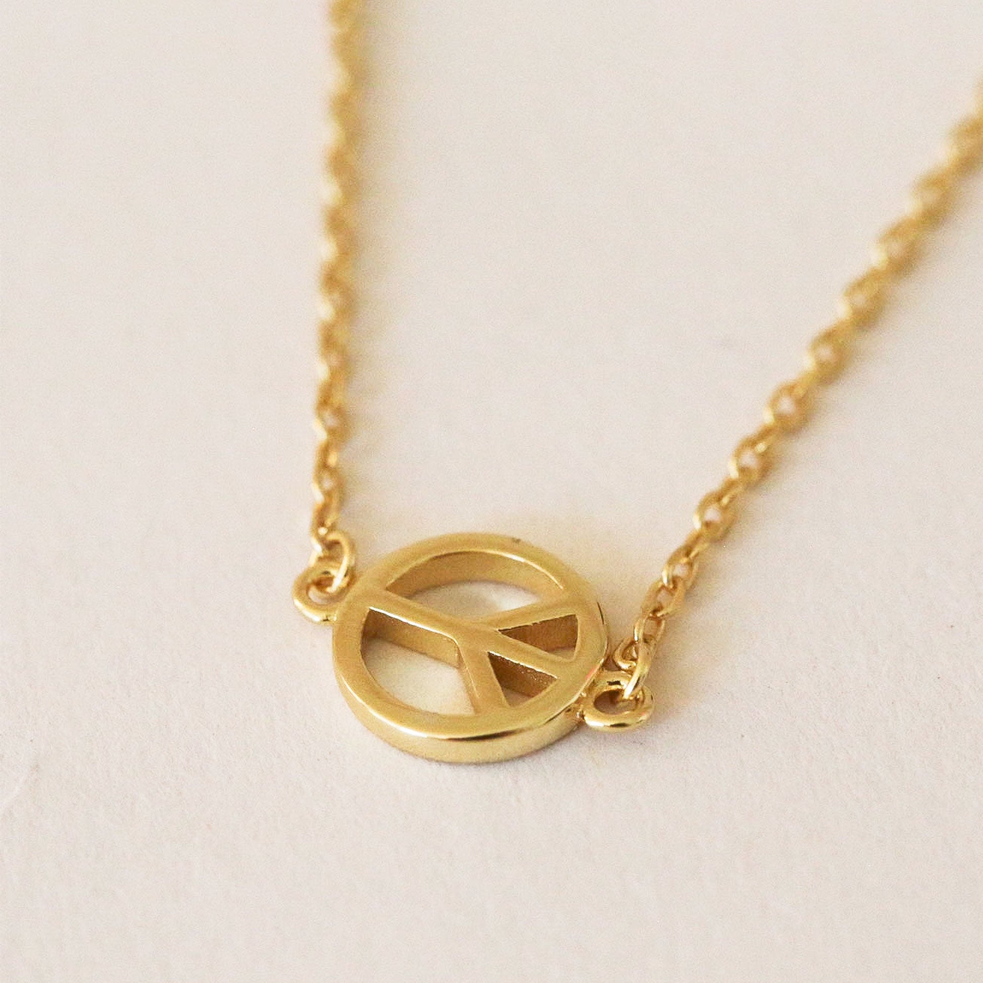 Gold chain necklace complete with classic peace sign symbol pendant. The pendent is connected to the chain by two loops on each side. 
