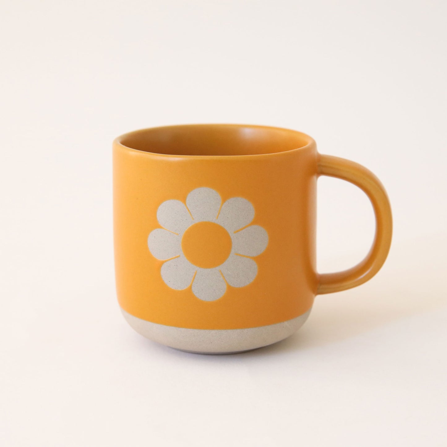 Natural clay mug painted tangerine orange with silhouette of classic daisy flower on the front. The base of the mug is unpainted, revealing natural clay. 