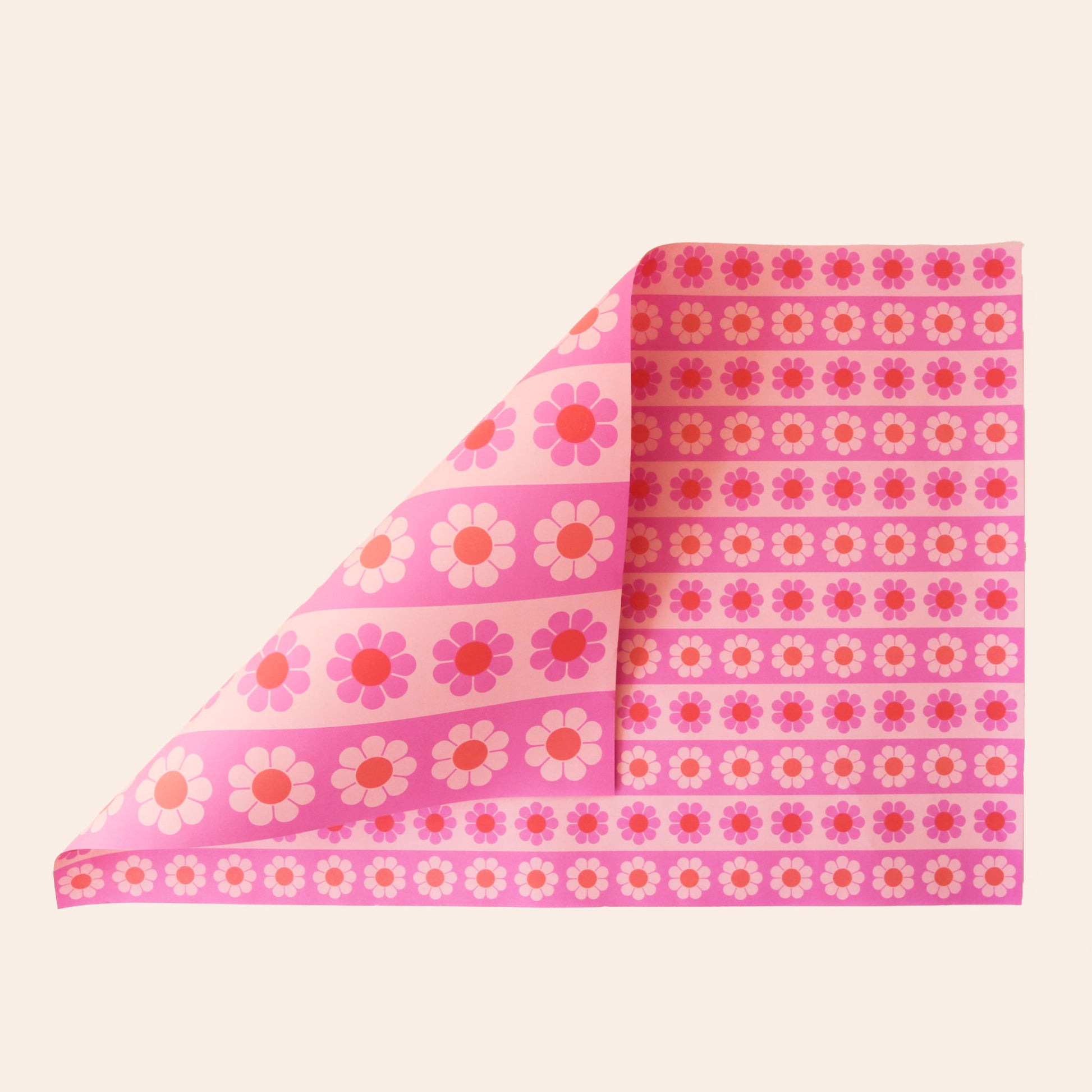 Sheet of wrapping paper filled with stripes of pink and orange flowers. The sheet is bent forward, revealing the other side of the wrapping paper. The back side is covered in larger stripes of the same floral print.