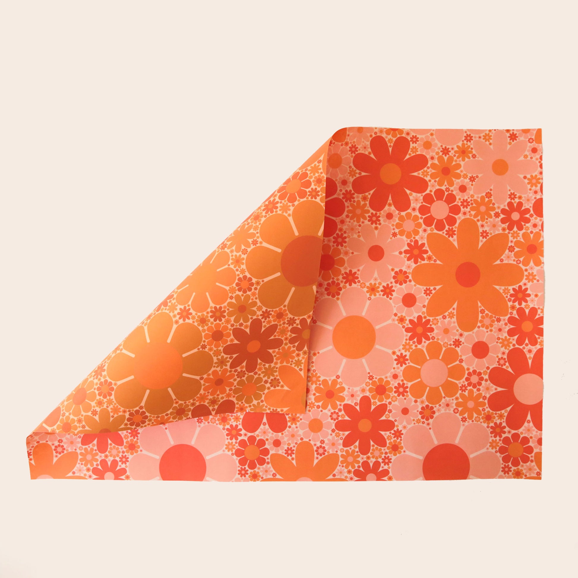 Sheet of wrapping paper filled with orange and pink flowers. The sheet is bent forward, revealing the other side of the wrapping paper. The back side is covered in the same floral print in oranges and yellows.