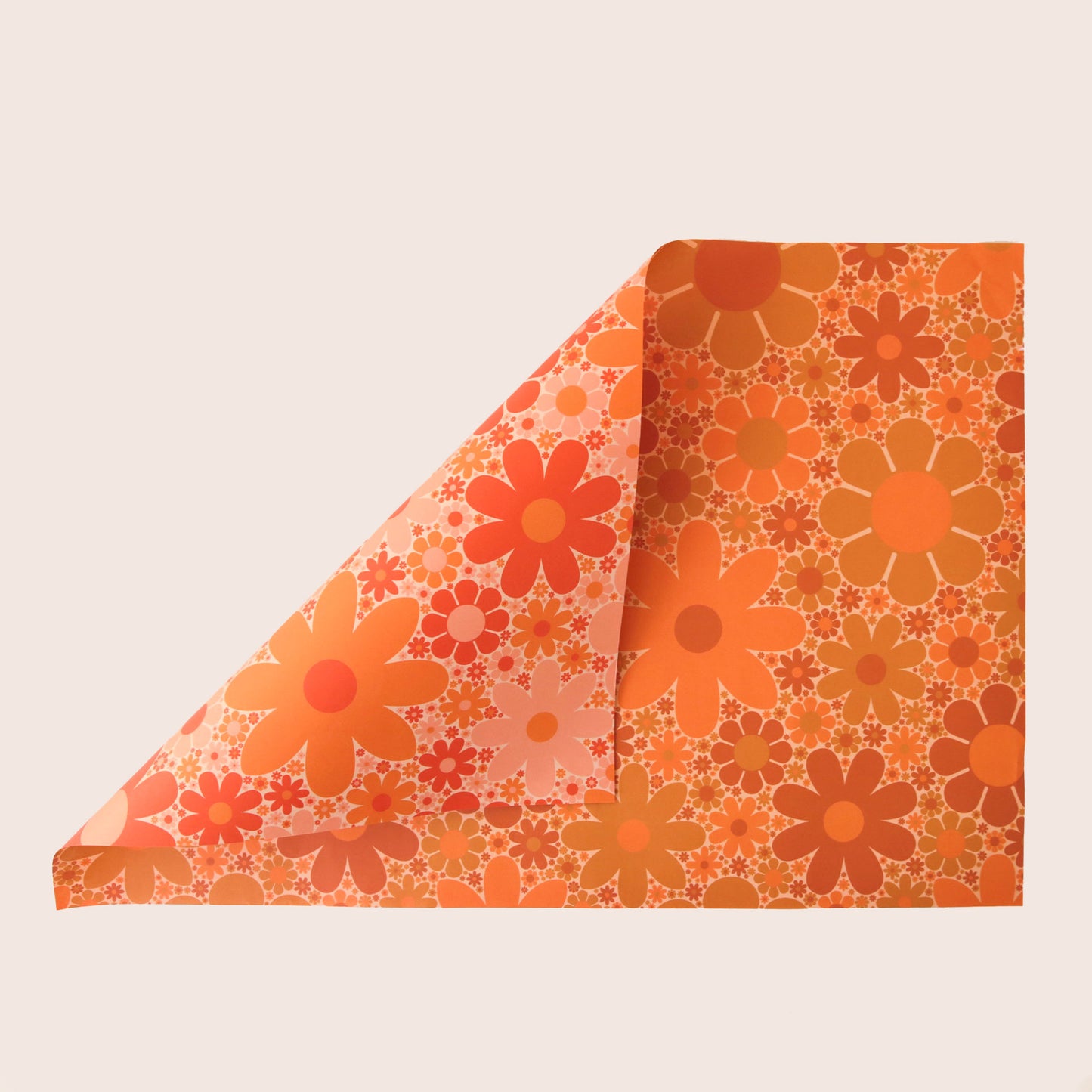 Sheet of wrapping paper filled with orange and yellow flower print. The sheet is bent forward, revealing the other side of the wrapping paper. The back side is covered in the same floral print in pink and oranges.