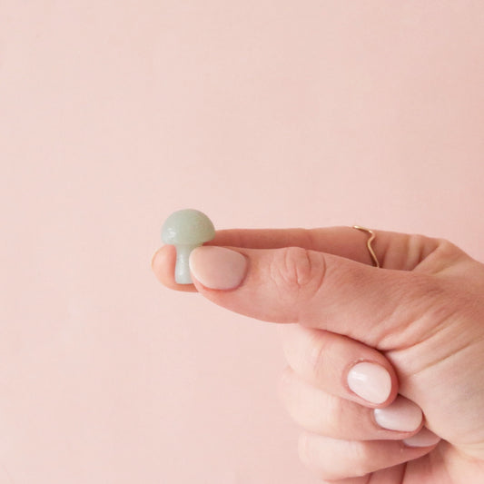 On a pink background is a tiny mushroom shaped Amazonite crystal being held by a model.
