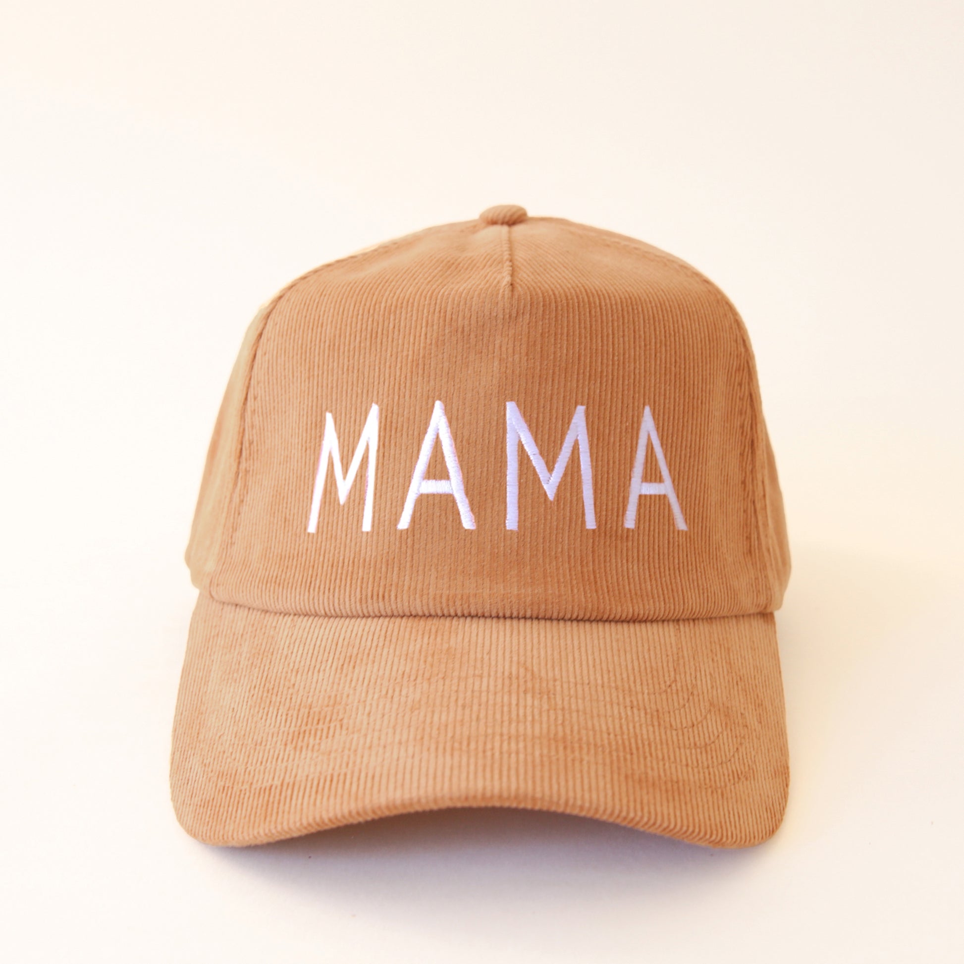 On a cream background is a burnt orange corduroy baseball hat with straight white capital letters that read, "MAMA" across the front.