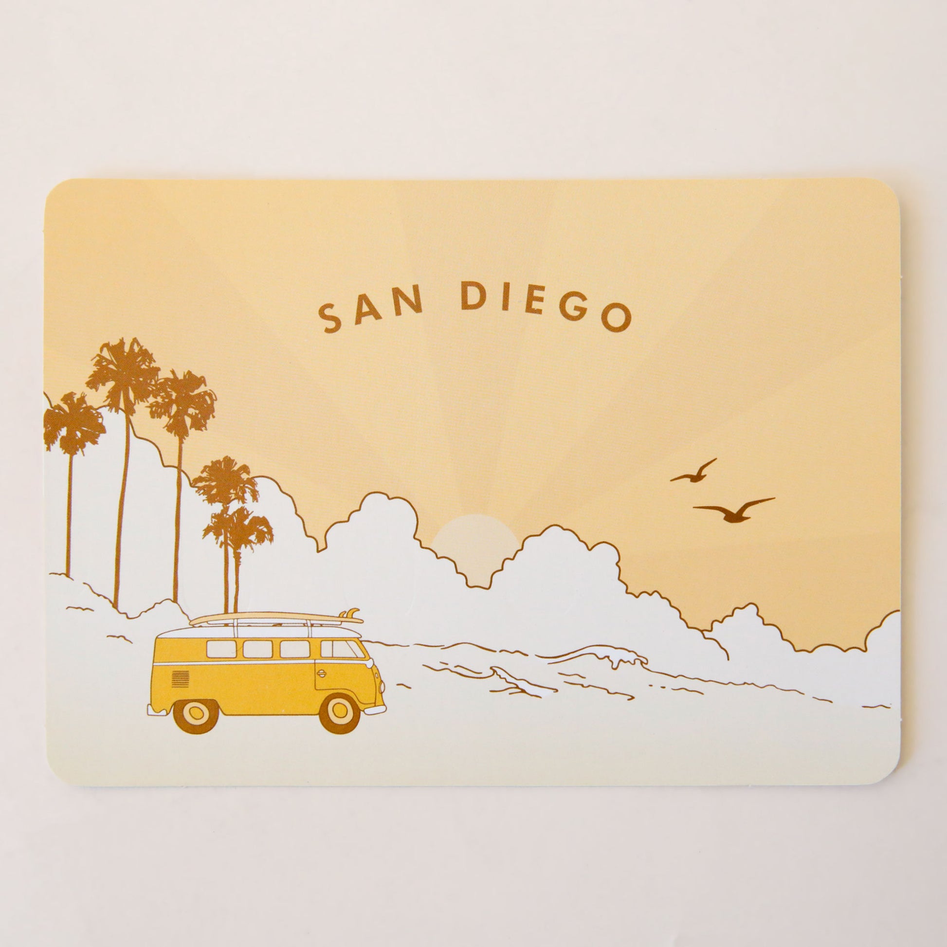 A peach postcard with palm trees and a VW bus with surfboards on the top of it. The text says, "San Diego".