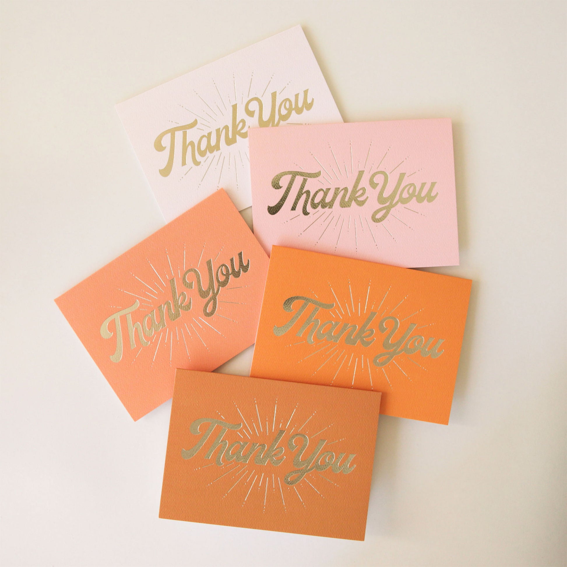 A pack of five different colored folded thank you cards with gold cursive font on the front that reads, "Thank You" along with gold line detailing. The colors range from ivory to light pink to terracotta.