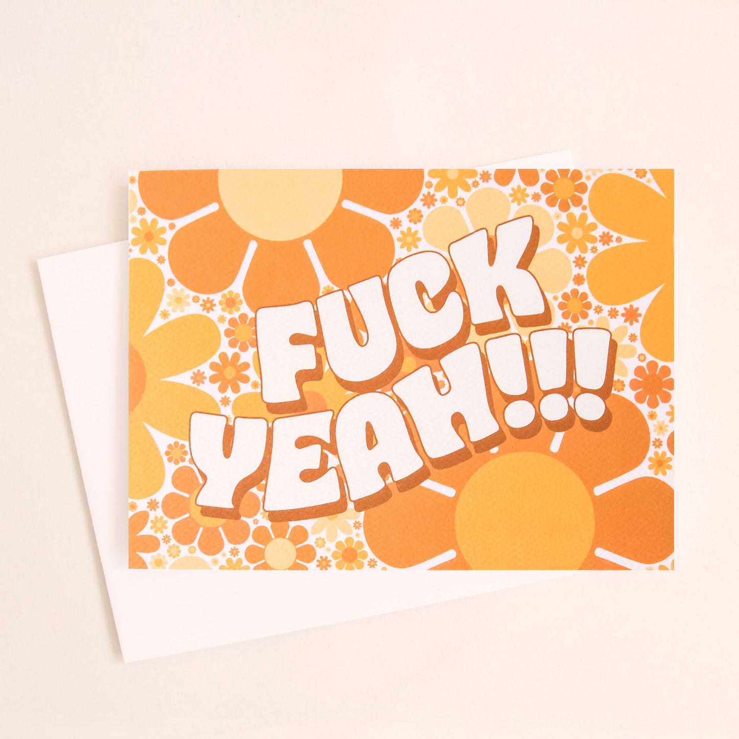Greeting card filled with retro yellow and orange flowers. The card reads 'fuck yeah!!!' in curved white bubble lettering. The card is accompanied by a solid white envelope. 