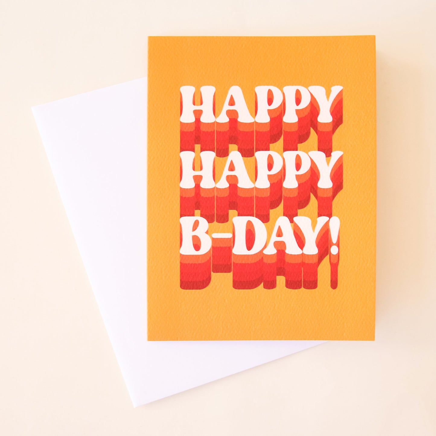 Mustard yellow card that reads 'happy happy b-day!' in white lettering. The letters are accented with orange and red detailing. The card is accompanied by a solid white envelope.