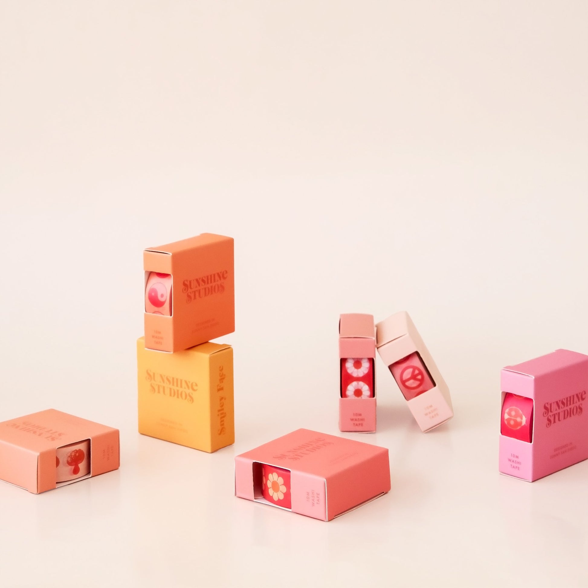 Seven warm toned square boxes of washi tape. The boxes are orange, yellow and pink displayed against a white background.