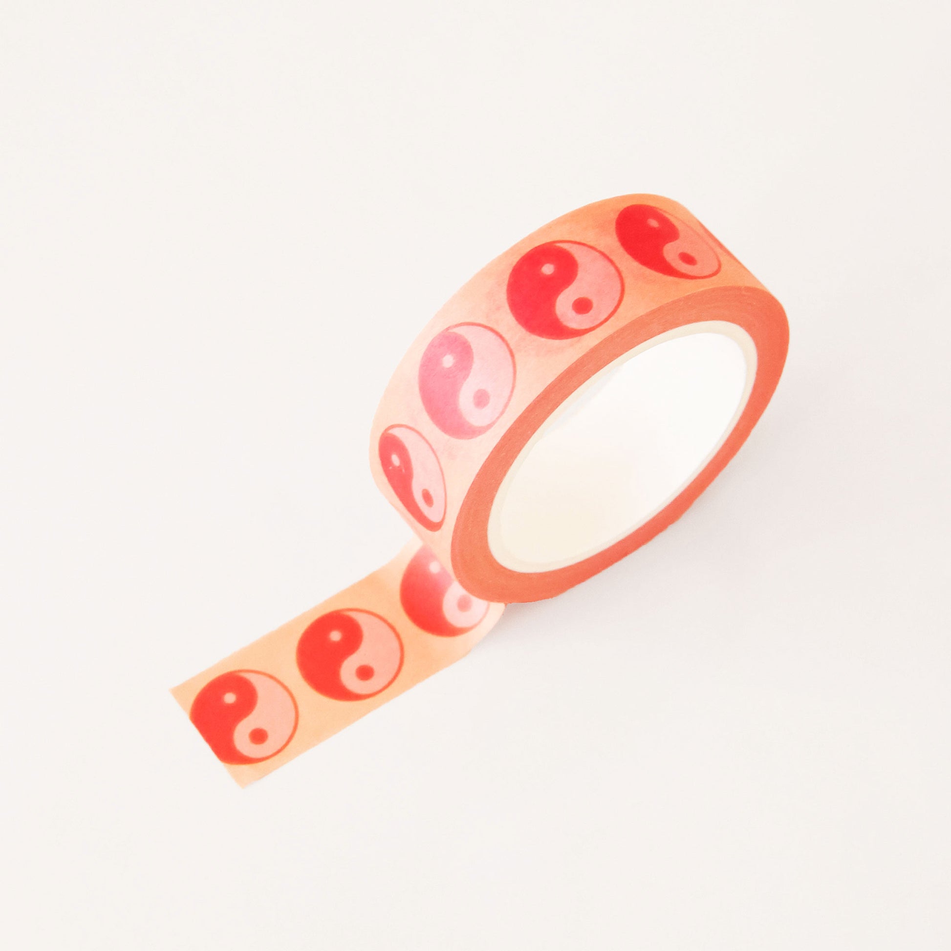 Roll of peach washi tape covered in red and pink yin-yang symbols. The roll is position upright, partially unrolled. 