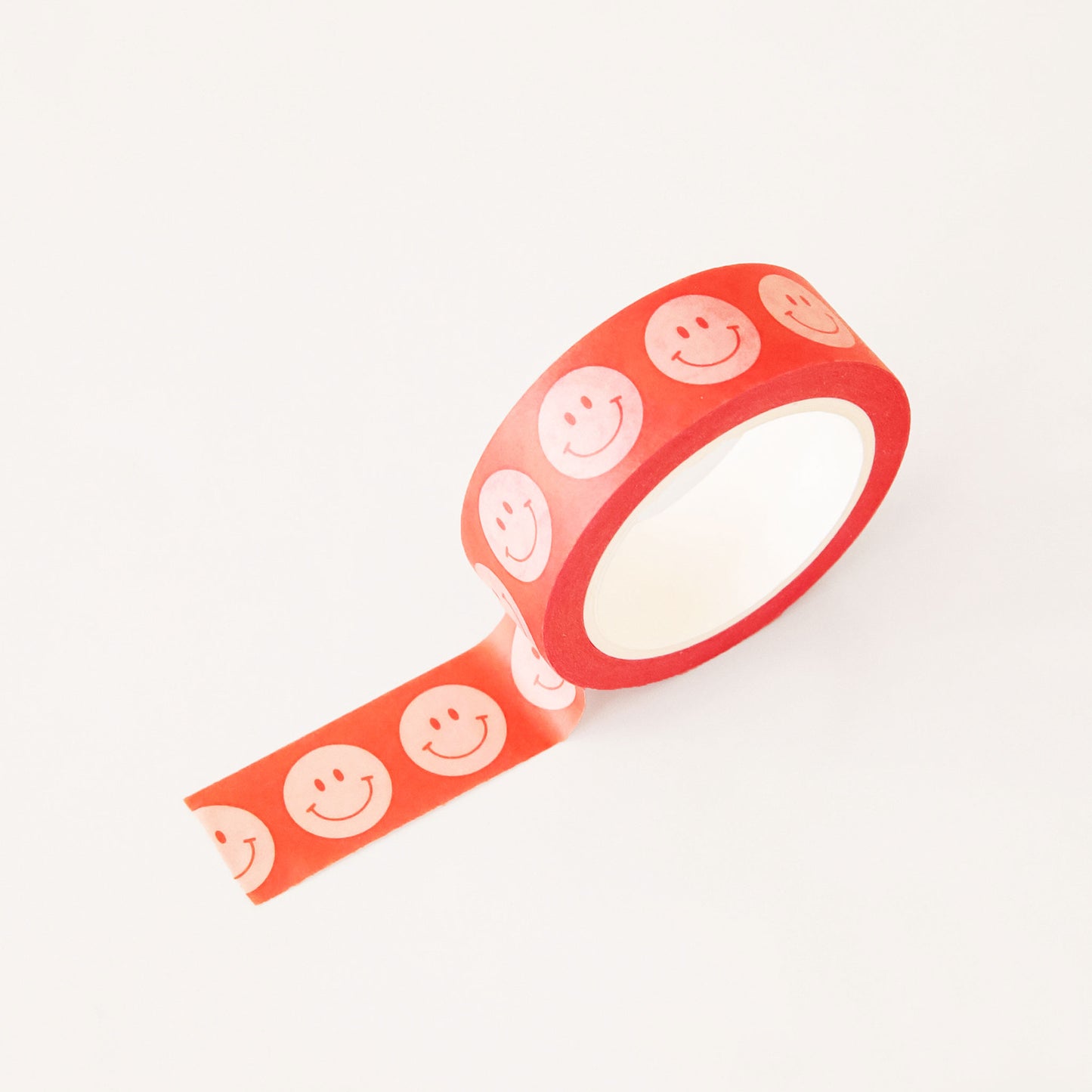 Roll of red washi tape covered in white classic smiley faces. The roll is position upright, partially unrolled.