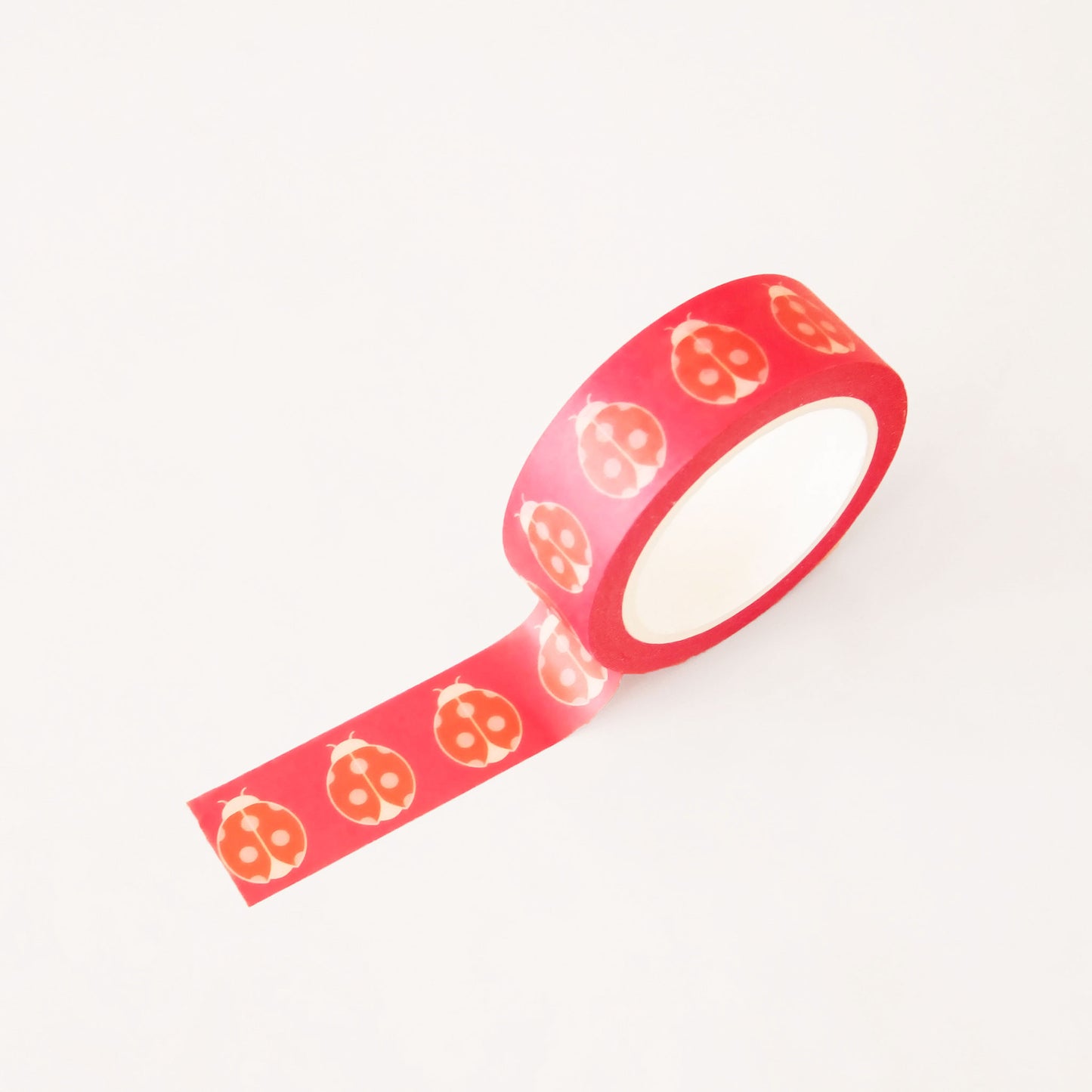 Roll of pink washi tape covered in red ladybugs. The roll is position upright, partially unrolled.
