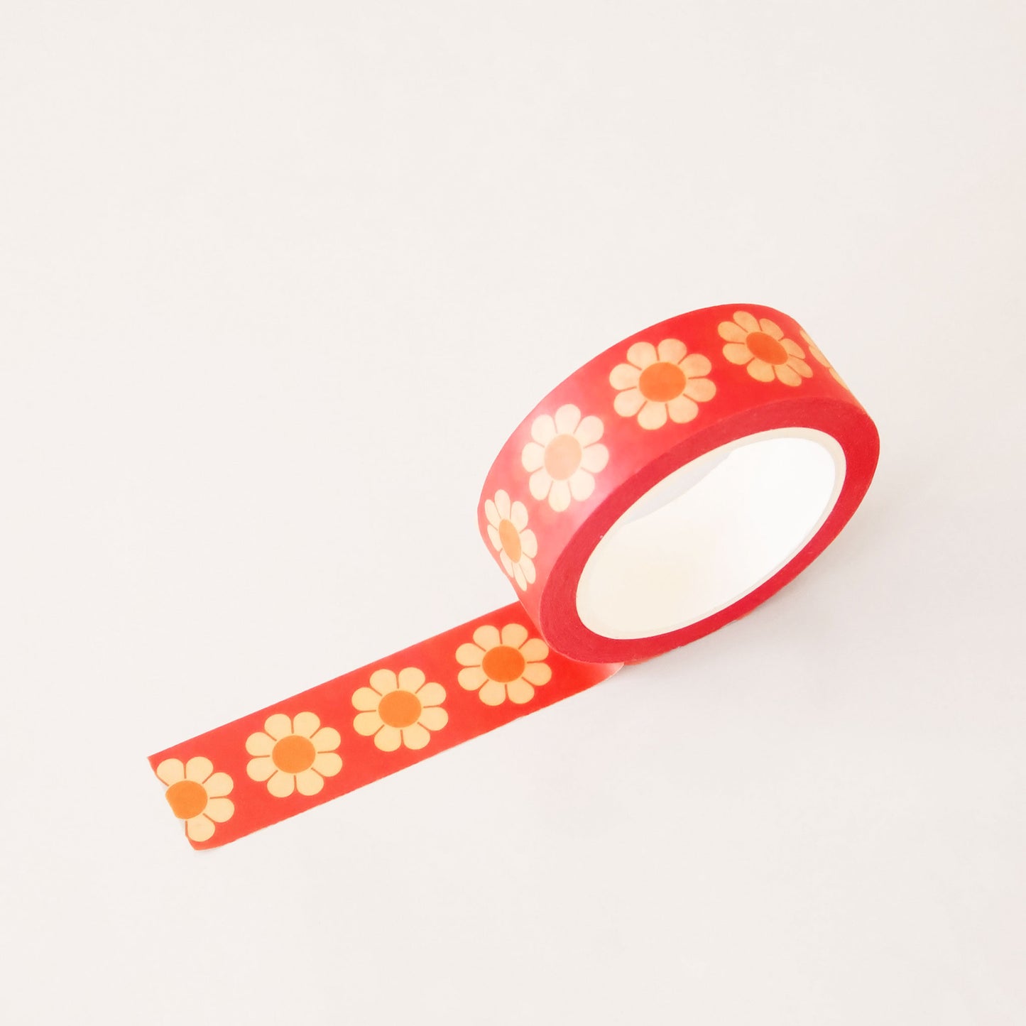 Roll of red washi tape covered in retro yellow and orange flowers. The roll is position upright, partially unrolled.