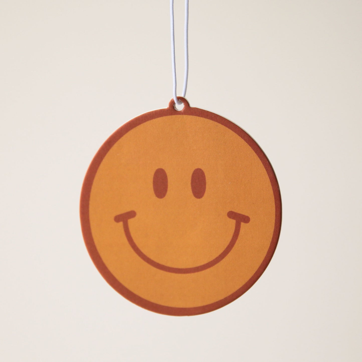 A burnt yellow car air freshener in the shape of a smiley face.