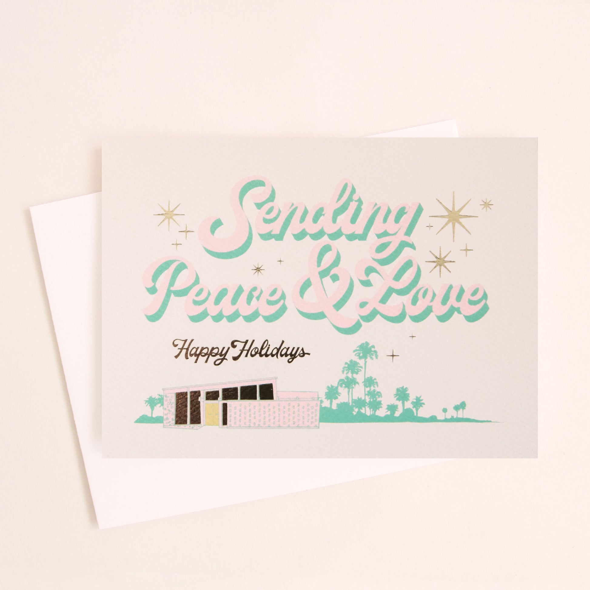 Cream card reading 'Sending Peace & Love' in soft pink lettering with seafood shadowing. Below reads 'Happy Holidays' in black cursive lettering. Below is a coastal scene of a pink beach house and sea foam palms.