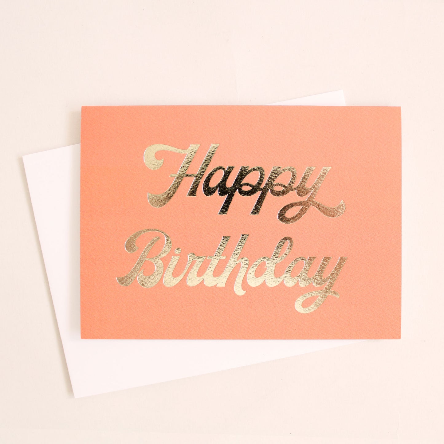 deep peached colored greeting card with gold foil text that reads happy birthday. Card is accompanied by a solid white envelope.