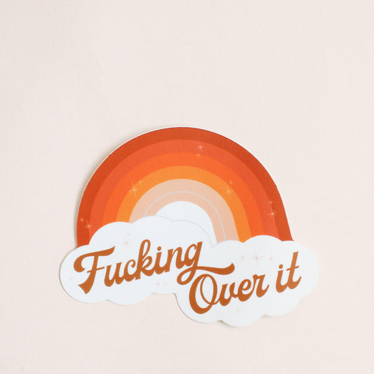 Bright rainbow designed sticker with dark orange sunset hues. This sticker reads 'Fucking Over It' in brown cursive lettering below the rainbow in white clouds.
