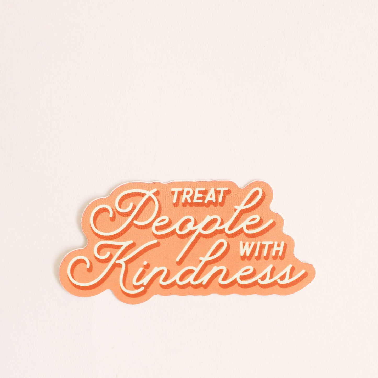 peach-orange sticker with white and dark orange text that reads treat people with kindness in white lettering. 