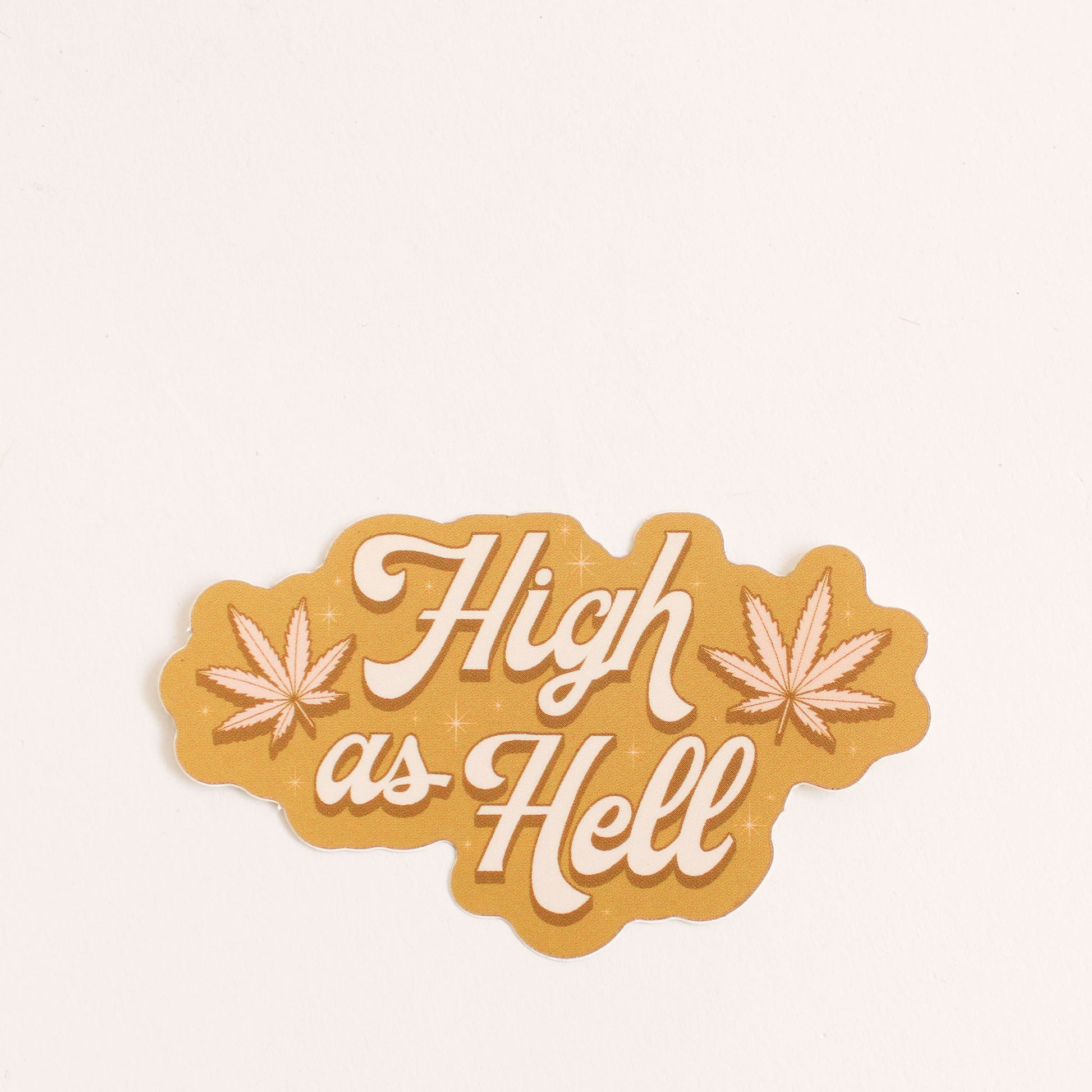 Deep gold sticker with two soft pink weed leaves and white cursive text that reads 'high as hell'.