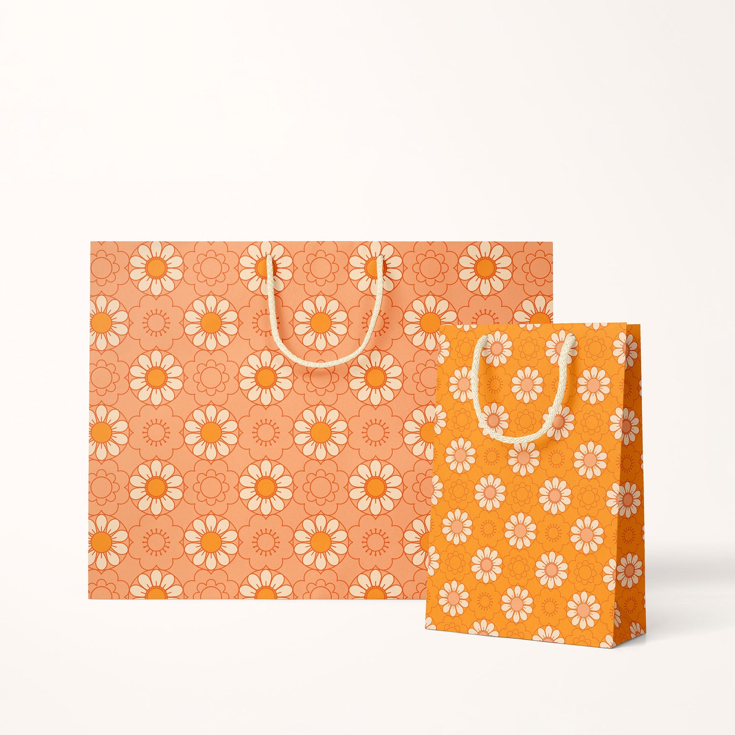 Two different sized paper gift bags with an orange background and a light yellow and orange repeating daisy print. They feature cotton string handles.